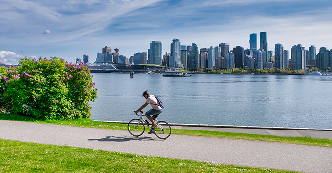 Person cycling along a waterfront bike path with the Vancouver skyline in the background on a sunny day Person cycling along a waterfront bike path with the Vancouver skyline in the background on a sunny day