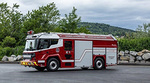 An electric fire truck parked with bushes and rocks in the background